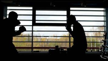 Silhouette of two boxers having a fight in a dark room in front of a window with sunlight. Stock footage. Side view of two fighters during sparring, sport concept. video