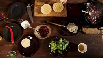 Top view of hamburger ingredients on a wooden table background. Stock footage. Chef hands cooking and using camembert cheese, red chili pepper, parsley, celery, and sauces, time lapse effect. video