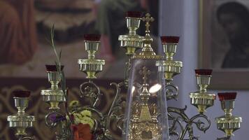 stänga upp av ett gammal menora i kyrka. stock antal fot. detaljer av interiör inuti av ortodox tempel, skön ljusstake med en korsa och blommor på suddig ikoner bakgrund. video