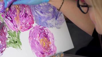 kunst schilderij met palet mes in de werkplaats. voorraad filmmateriaal. dichtbij omhoog van een vrouw in bril schilderij mooi roze bloemen met een professioneel hulpmiddel. video