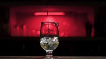 Pouring fresh alcoholic drink into the glass with ice cubes on the bar counter. Stock footage. Close up of process of cocktail preparation, adding blue syrup into the glass. video