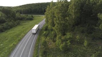 Aerial view of the concrete road and green grass and trees growing along it, white wagon with goods moving on the empty road. Scene. Transport and freight services concept. video
