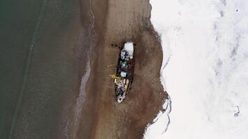 oben Aussicht von segeln Schiff zerstört auf das Küste im Antarktis. Filmaufnahme. fliegend über das Winter schneebedeckt Küste durch das Meer und das alt rostig Schiff. video