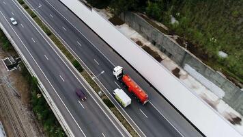 aéreo ver de el la carretera con Moviente carros y un camión a lo largo el montaña Pendiente cubierto por verde arboles escena. parte superior ver de ferrocarril y automóvil la carretera con Moviente vehículos video