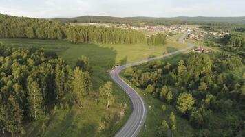 aereo di il vuoto strada andando attraverso foresta, estate natura paesaggio. scena. volante sopra il autostrada attraverso il verde abete rosso foresta con blu nuvoloso cielo e piccolo villaggio su il sfondo. video