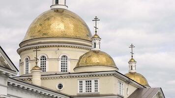 skön arkitektonisk Fasad av de kristen kyrka med gyllene kupoler. stock antal fot. vit väggar av kyrka med gyllene kupoler på bakgrund av molnig himmel video