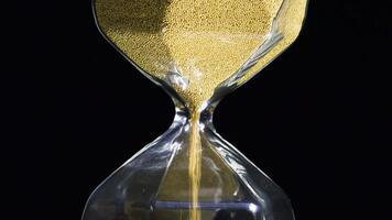 Close-up of golden hourglass. Stock footage. Stylish hexagon hourglass with falling gold specks on black isolated background. Passage of time and importance of every grain video