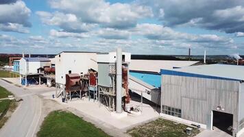 antenne visie van cement productie fabriek met magazijnen Aan blauw bewolkt lucht achtergrond. voorraad filmmateriaal. vliegend bovenstaand industrieel zone en cement productie fabriek, zwaar industrie concept. video