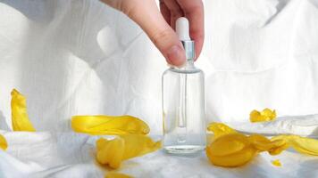 Close up of transparent glass bottle of cosmetic oil surrounded by yellow tulip petals on white background. Concept. Cosmetology and beauty, woman hand taking away small vial. video