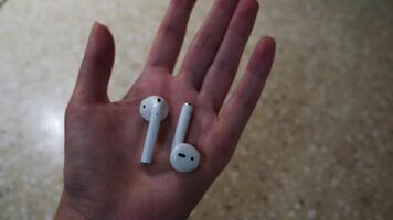 Close up of woman hand holding air pods. Concept. Wireless headphones of white color in female hands on beige table background. video