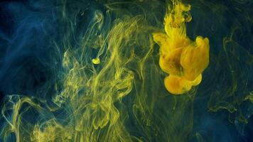 Beautiful yellow paint drops spreading in water. Stock footage. Close up of clouds of yellow and blue ink isolated on black background, art concept. video