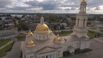 Aerial view of the beautiful white church with a tower and gold domes, religion and faith concept. Stock footage. Flying over the church with city buildings and blue cloudy sky on the background. video