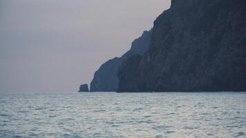 sera bellissimo paesaggio con rocce, volante gabbiano e piccolo mare onde. sparo. naturale sfondo di il tramonto al di sopra di il increspato mare superficie e il montagne. video