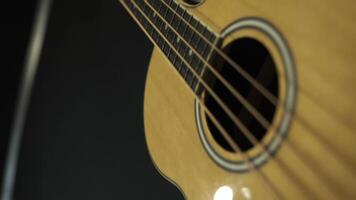 vicino su di classico chitarra con acciaio stringhe su nero sfondo, musica concetto. azione filmato. parte inferiore Visualizza di di legno acustico chitarra, nuovo strumento. video