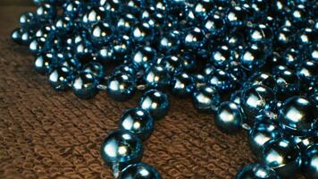 Close up of beads of blue color for decoration. Stock footage. Shining beautiful garland made of connected small blue balls with eflecting surface lying on a brown carpet, Christmas and New Year video