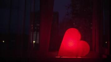 Nightlight in the shape of a heart in the children room. Concept. Red beautiful heart shaped night lamp turned on while standing on windowsill in front of window. video