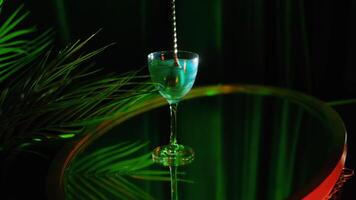 Close up of Aviva green wine with pearl standing on a glass surface table near the plant under green light. Stock footage. Composition in green colors and a hand stiring shining wine with a spoon. video