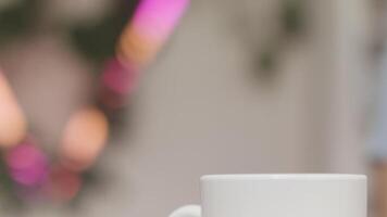 Close up of a woman hands throwing sugar into a white mug with hot beverage on blurred background. Stock footage. Female hands adding white sugar into tea or coffee. video