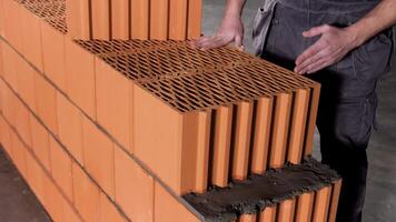 Close up of a worker standing at the unfinished red brick wall and drawing a line with his hand for further actions. Stock footage. Detail of worker and layers of bricks. video