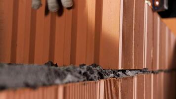 Industrial worker building exterior walls with orange bricks and mortar. Stock footage. Bricklayer putting down another row of bricks. video