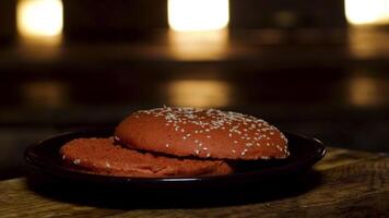 cerca arriba de hamburguesa bollos acostado en un plato en oscuro habitación antecedentes. valores imágenes. Cocinando y preparación de hamburguesa, recién horneado bollos con sésamo semillas video