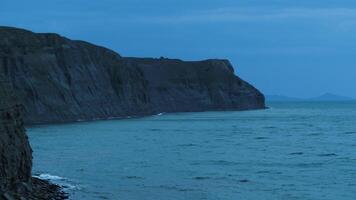 étourdissant paysage marin avec une raide falaise sur foncé bleu ciel Contexte. tir. soir à le mer Coût avec petit vagues et rochers. video