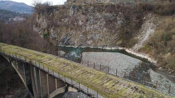 Aerial of mountainous landscape of old abandoned stone bridge over cold stream near steep cliffs. Shot. Flying over the bridge leading nowhere. video