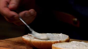 fechar acima do masculino chefe de cozinha mão com uma colher de chá adicionando branco maionese molho em uma Hamburger pão. estoque imagens de vídeo. preparação do delicioso hambúrgueres às lar. video