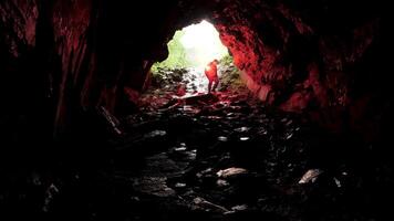 silhouette de une homme avec rouge brûlant signal éclater à l'intérieur une caverne entrée. Stock images. découvrir dangereux souterrain chemin. video