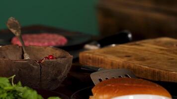 Close up of the ingredients on the wooden table. Stock footage. Beef cutlet, cranberries in wooden bowl, greenery, and burger bun near wooden board. video