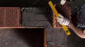 Top view of an industrial worker making wall with mortar and bricks, using hammer and level tool. Stock footage. Male hands building exterior walls, using hammer for laying bricks in cement. video