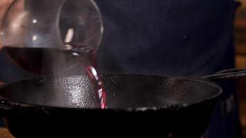 scrosciante rosso vino in frittura padella. vicino su di capocuoco maschio mani aggiungendo rosso vino in nero ferro padella per cucinando speciale salsa. video