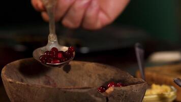 hölzern alt Schüssel mit Preiselbeeren Stehen auf das Tabelle auf dunkel Zimmer Hintergrund. Lager Filmaufnahme. schließen oben von männlich Hand nehmen ein Löffel von rot frisch Beeren zum Kochen. video