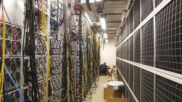 Close-up of data center of the large company with lots of fans, system units and wires and young network administrator pluging in wires. Stock footage. IT professionals concept video