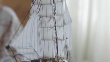 Close-up of the little marine white ship model from the wood on a striped background on the blurred light background. Stock footage. Hobby and collecting concept video