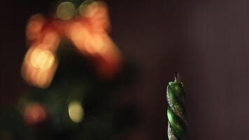 Close-up of lighted and extinction Christmas candle against the blurred Christmas tree silhouette with lights and decorations. Concept. Christmas mood video