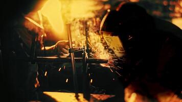 Close up of workers in a welding masks and protective gloves using welding machine in the dark workshop with bright sparks flying into the sides. Stock footage. Workers with professional equipment. video