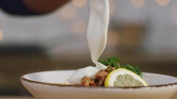 Close-up of some person's hand adding sour cream at the bowl with solyanka. Stock footage. Russian solyanka soup with meat, sausages and olives video