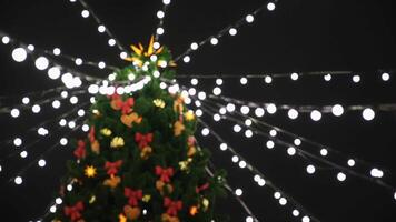 Aussicht von das Unterseite auf das schön Weihnachten Baum mit bunt Dekorationen und Girlande von Weiß Beleuchtung Stehen auf das Quadrat. Konzept. schön schneebedeckt Winter Landschaft von Weihnachten Urlaub video