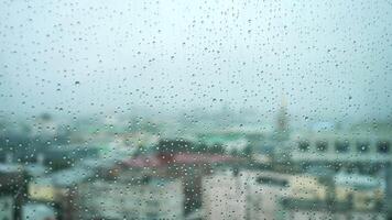 View of the city through the window and raindrops falling down on the glass. Stock footage. Autumn weather video