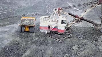 Top view of excavator in open pit. Excavator falls asleep rubble in dumper on outdoor quarry in extraction of minerals. Concept of extraction of minerals video