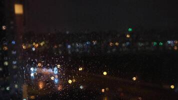 ver de el borroso ciudad mediante el ventana y gotas de lluvia que cae abajo en el vaso a el noche. concepto. lluvioso clima video