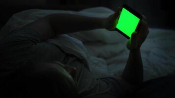 hombre usos teléfono mientras acostado en cama. concepto. joven hombre acostado en cama usos teléfono inteligente con verde pantalla. dependencia en teléfonos inteligentes y social redes video