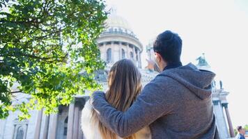 casal abraços e parece às catedral. conceito. lindo casal em período de férias olhando às histórico vistas do cidade. costas Visão do homem e mulher em fundo verde árvore e catedral dentro Sol video