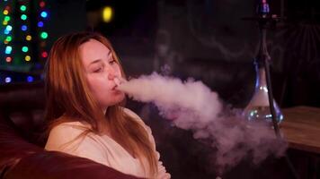 femelle fumeur avec narguilé sur foncé Contexte de nuit club intérieur. médias. plus Taille magnifique modèle avec une mal habitude de fumeur chicha, concept de loisir et se détendre. video