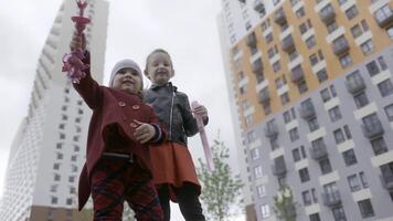 Lovely girls blowing bubbles, bottom view. Action. Female caucasian children dressed in warm clothes creating many soap bubbles in spring time on multi storey buildings background. video