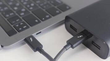 Black portable external power bank, for emergency device recharge. Action. Close up of an open laptop is charged with a power bank via a cable, portable modern devices, external battery, cable, USB video