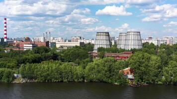 antenne visie van een groot modern stad en de vijver. video. vliegend over- de zomer water reservoir in de buurt industrieel wijk van de stad met schoorstenen en veel groen bomen Aan blauw bewolkt lucht achtergrond. video