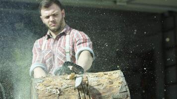 ritratto di caucasico giovane uomo lavoratore segare un' log con un' motosega. video. maschio falegname segare un' parte di albero tronco con di legno trucioli volante in il lati. video