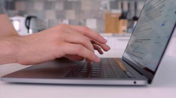 Close up of man hands typing on laptop keyboard. Action. Side view of male hands and his laptop on blurred background of a kitchen, business and communication concept. video